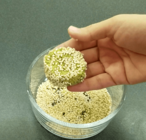 pressing raw falafel patties into sesame seeds before frying