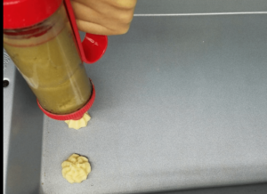 piping butter cookies dough into shapes on baking tray using star tip