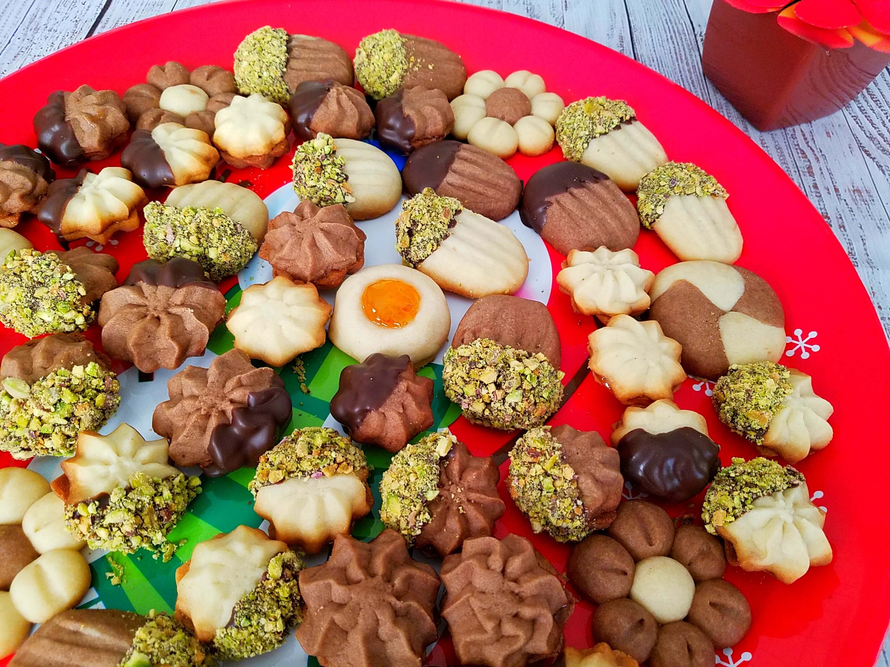 A beautiful close-up shot of a decorated Egyptian betefour cookie rosette tray, showcasing crisp piped-star edges, a layer of apricot jam filling, and half-dipped in chocolate and crushed pistachios.