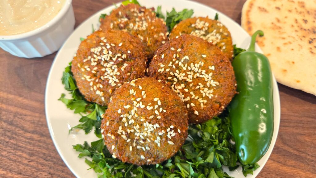 A premium close-up shot of crispy fried Egyptian falafel patties with tahini sauce and pita bread.