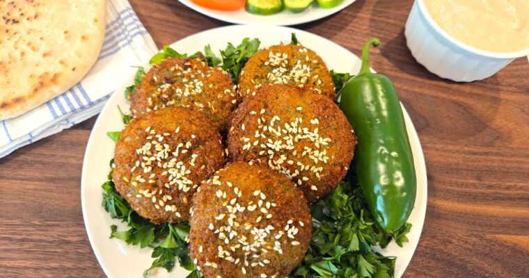 A wide overhead shot of a crispy golden brown Egyptian falafel platter, showcasing traditional Ta'ameya patties garnished with fresh herbs and sesame seeds.