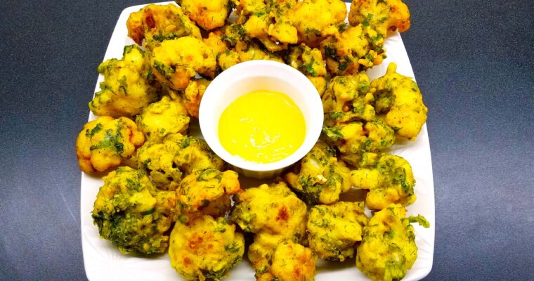 A wide overhead shot of a large serving platter with crispy golden brown Egyptian fried cauliflower florets, garnished with fresh chopped herbs and served with yellow mustard sauce.