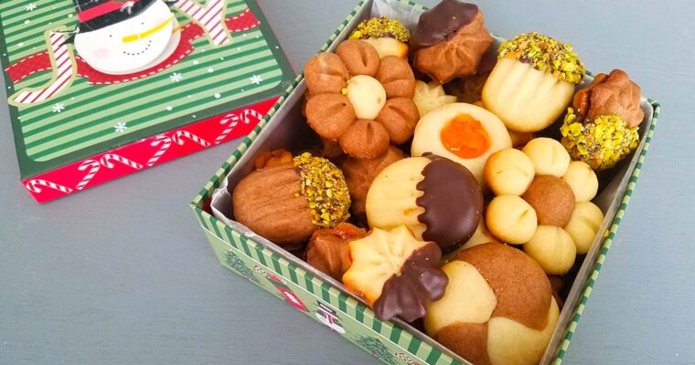 A gift box filled with decorated Egyptian Betefour cookies, showing piped vanilla and chocolate petit fours sandwiched with jam and dipped in chocolate and crushed pistachios.