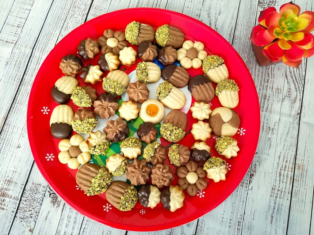 A tray of decorated Egyptian betefour cookies with apricot jam filling, and half dipped in chocolate and crushed pistachios.