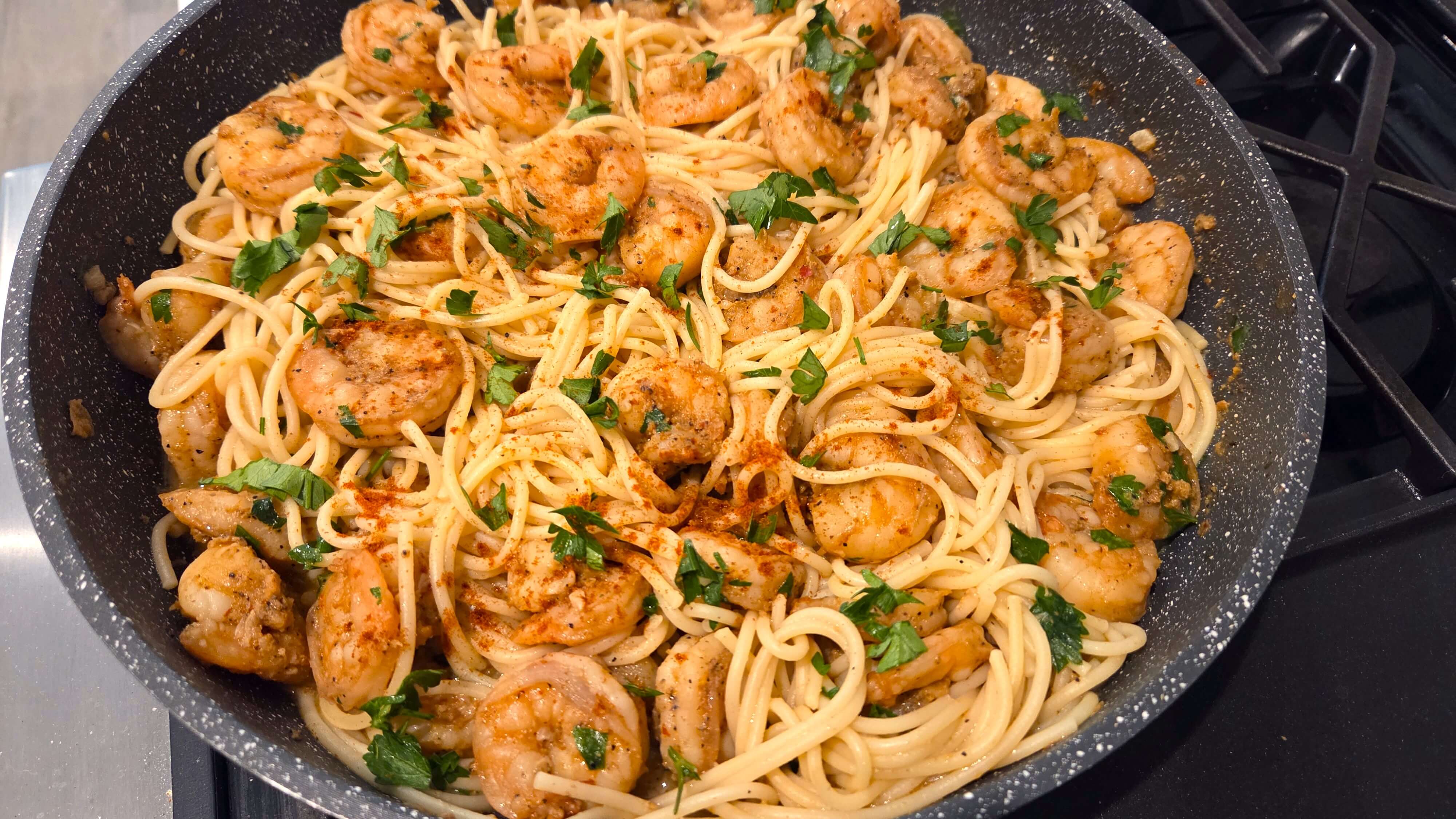 A skillet with Shrimp scampi pasta garnished with fresh chopped parsley.