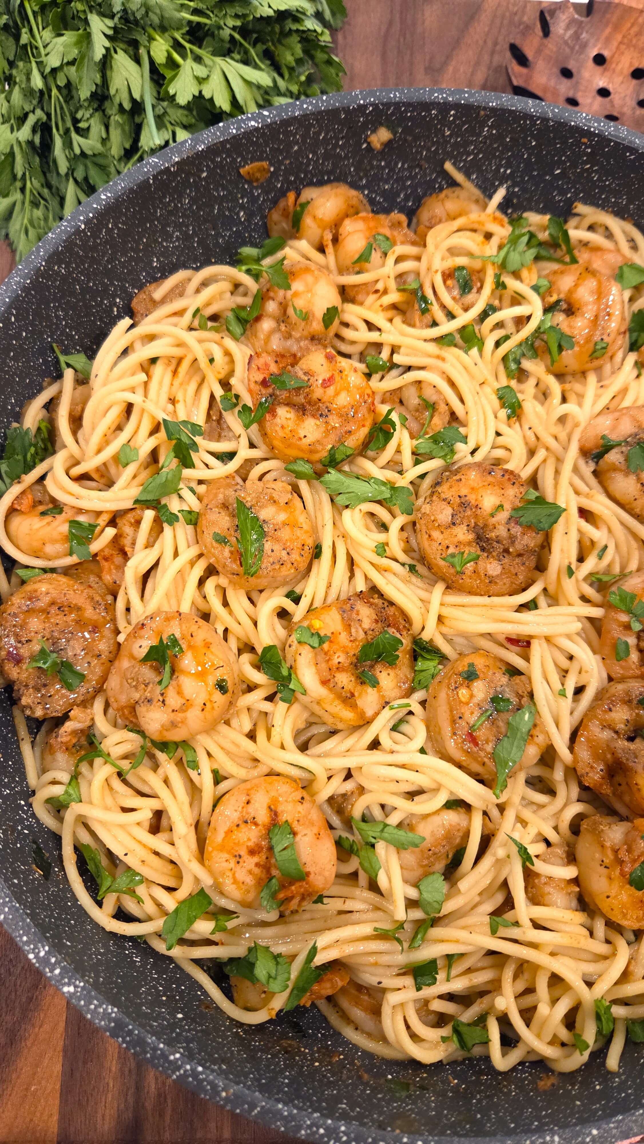 A close-up view of fresh large shrimp seared in a rich garlic butter sauce, mixed with spaghetti and fresh chopped parsley.