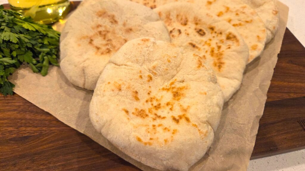 Warm homemade Egyptian pita bread stacked on a cutting board.