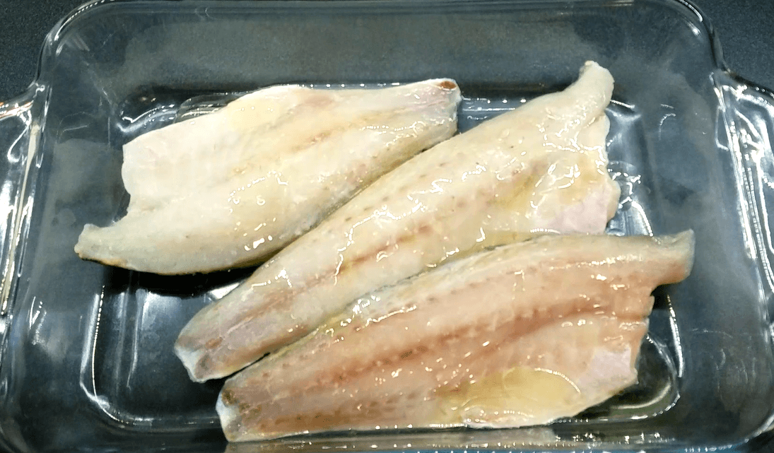 Olive oil and lemon juice drizzled over sea bass fillets in a baking dish