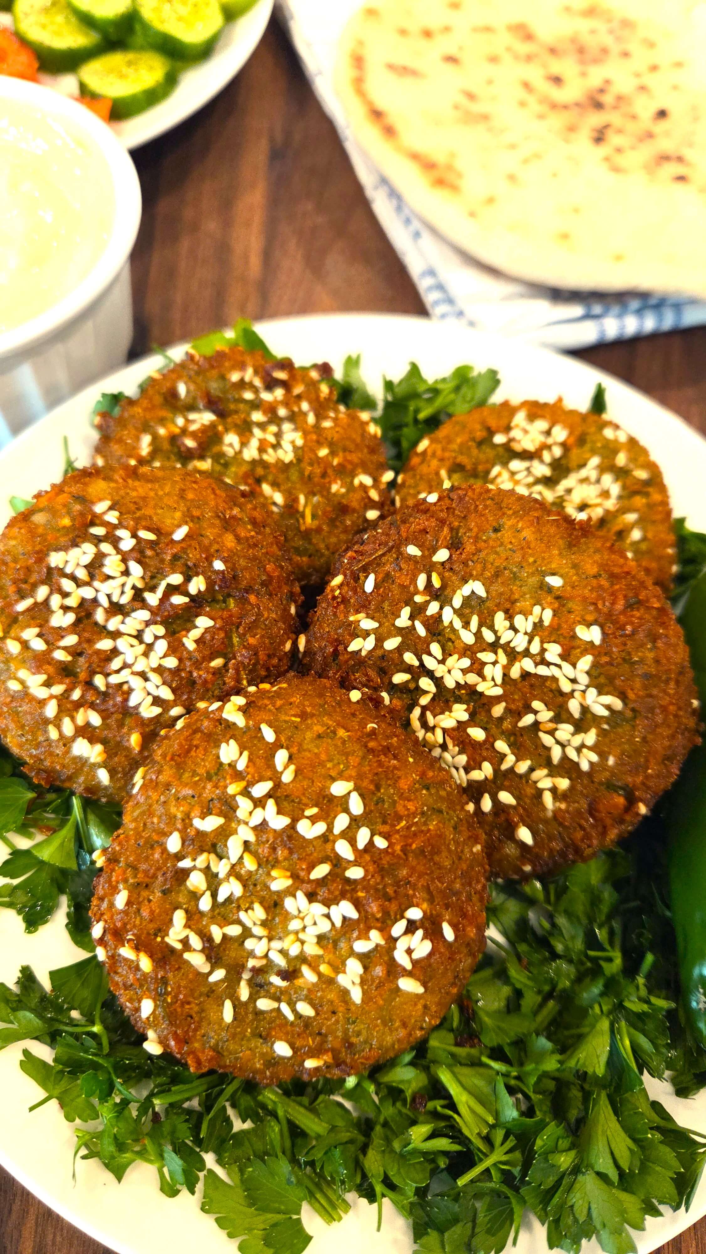 A beautiful close-up of crispy fried Egyptian falafel patties served with warm pita bread, creamy tahini sauce, fresh sliced tomatoes, and cucumbers.