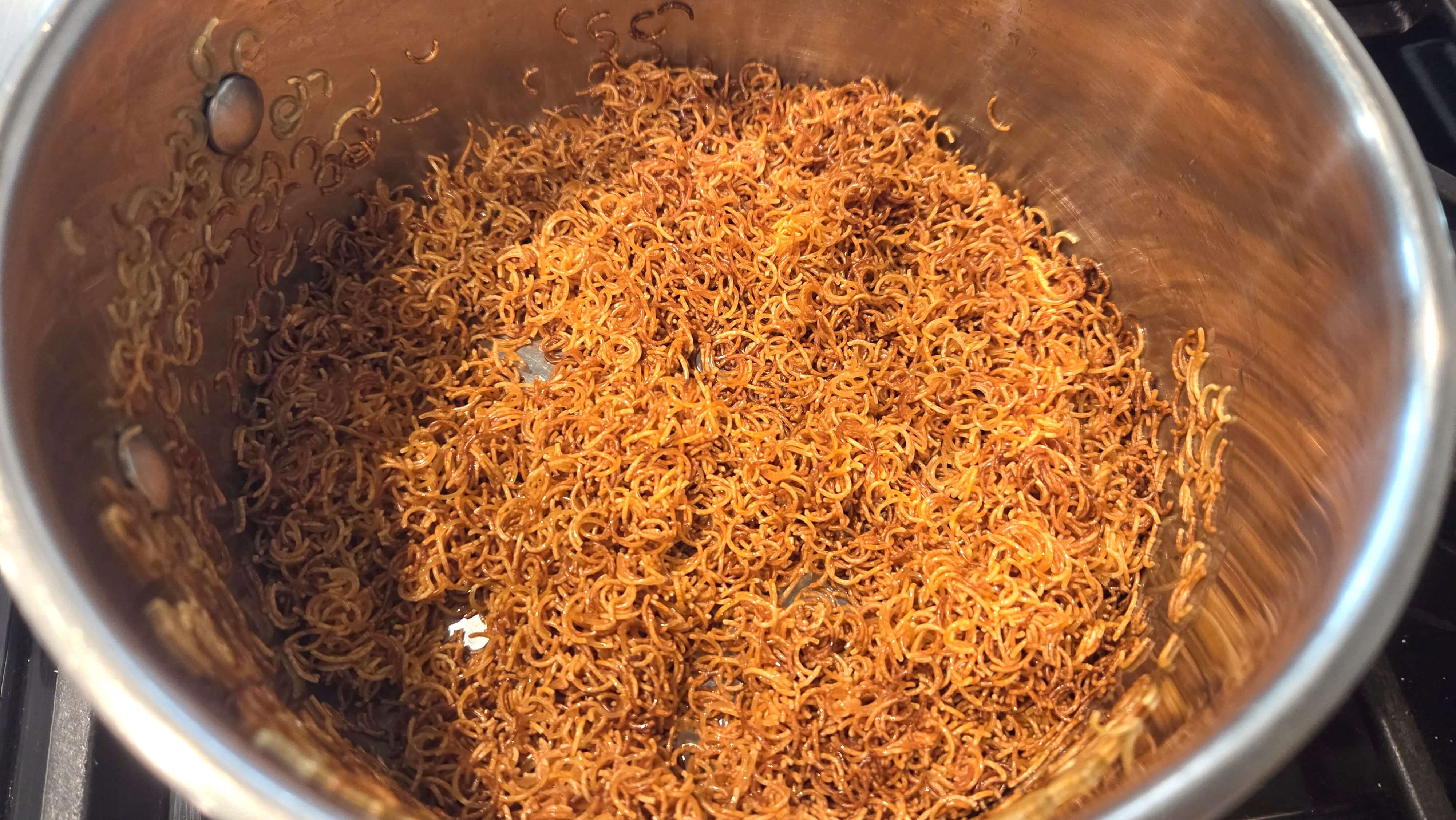 Browning broken vermicelli noodle strands in a hot pot with oil until they turn a deep, even copper-golden brown.
