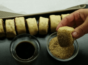 Dipping each cookie slice into molasses and sesame seeds