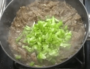Bell peppers on top of cooked beef liver strips in a skillet