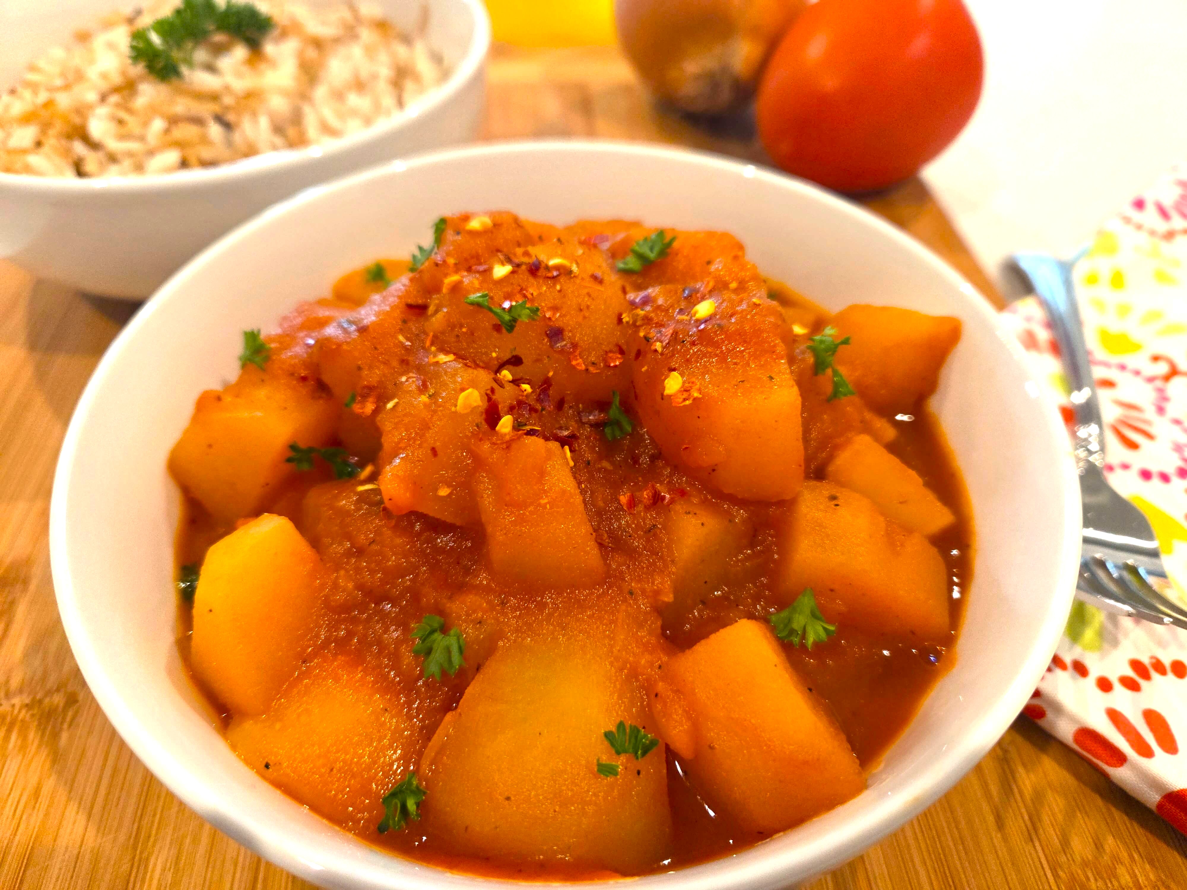 A premium close-up shot of a perfectly tender, buttery cubes of Egyptian potato stew in a deep serving bowl, showing the thick onion-infused sauce.