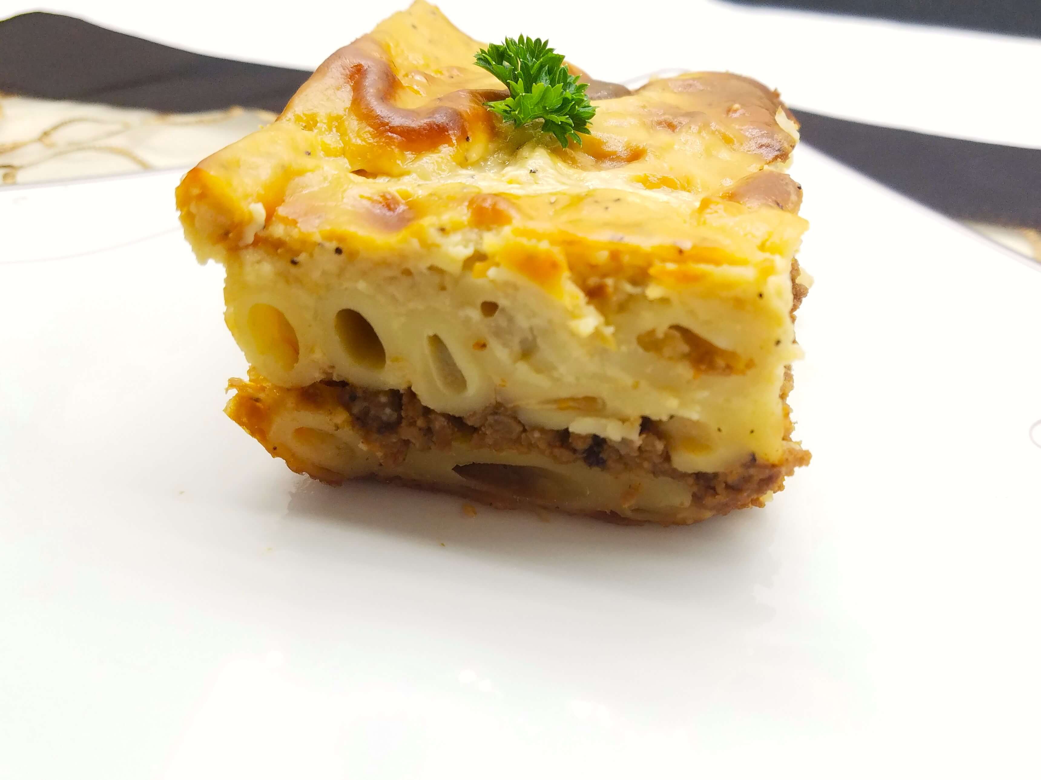 A premium close-up shot of a single serving of creamy Egyptian Macarona Bechamel, highlighting the melt-in-your-mouth texture of the rich baked white sauce over tender penne pasta.