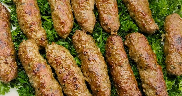 A wide overhead shot of a large serving platter piled with juicy, golden-brown Egyptian kofta kebabs on a fresh bed of chopped parsley.
