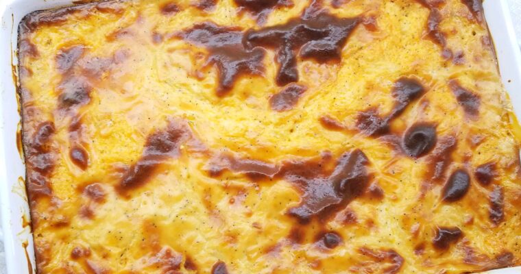 A wide overhead shot of a freshly baked Egyptian Macarona Bechamel casserole in a baking dish, showcasing an intensely rich bubbling golden brown cream crust.