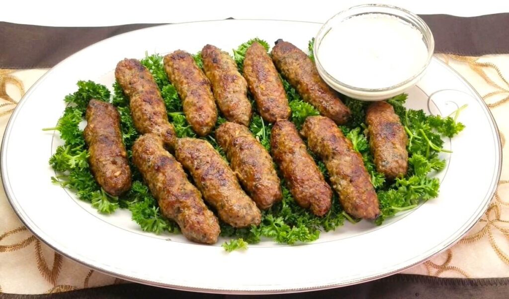 A beautiful close-up of a juicy street-style Egyptian kofta kebab with a small bowl of creamy tahini sauce.