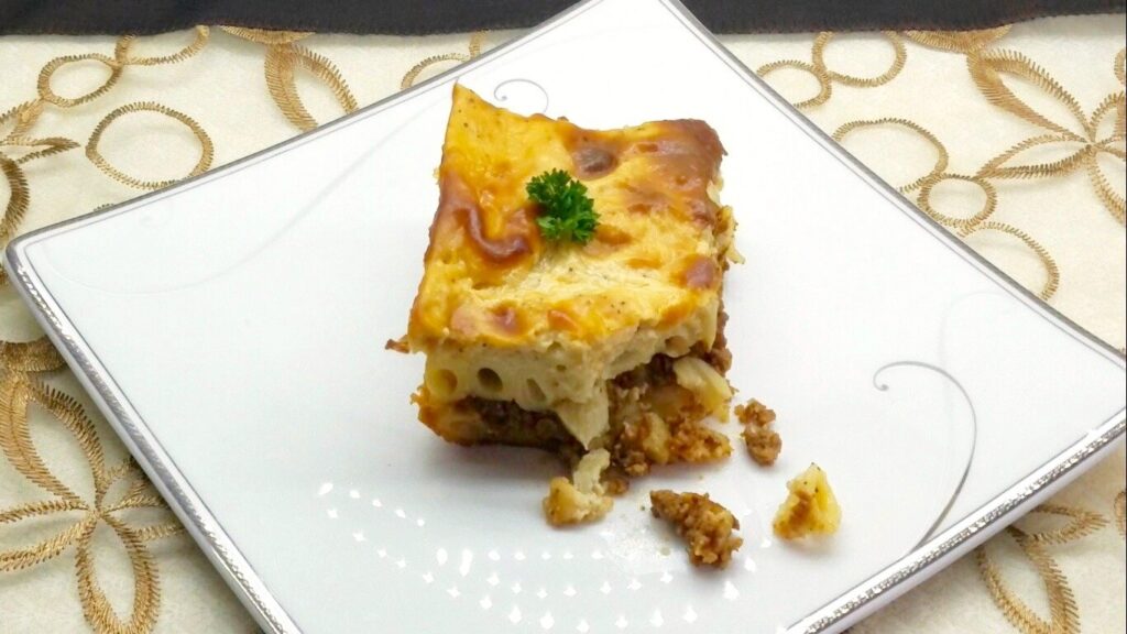 A perfectly cut square slice of Egyptian Macarona Bechamel showing clean distinct layers of penne pasta, spiced ground beef, and a thick velvety white sauce crust on a decorative serving plate.