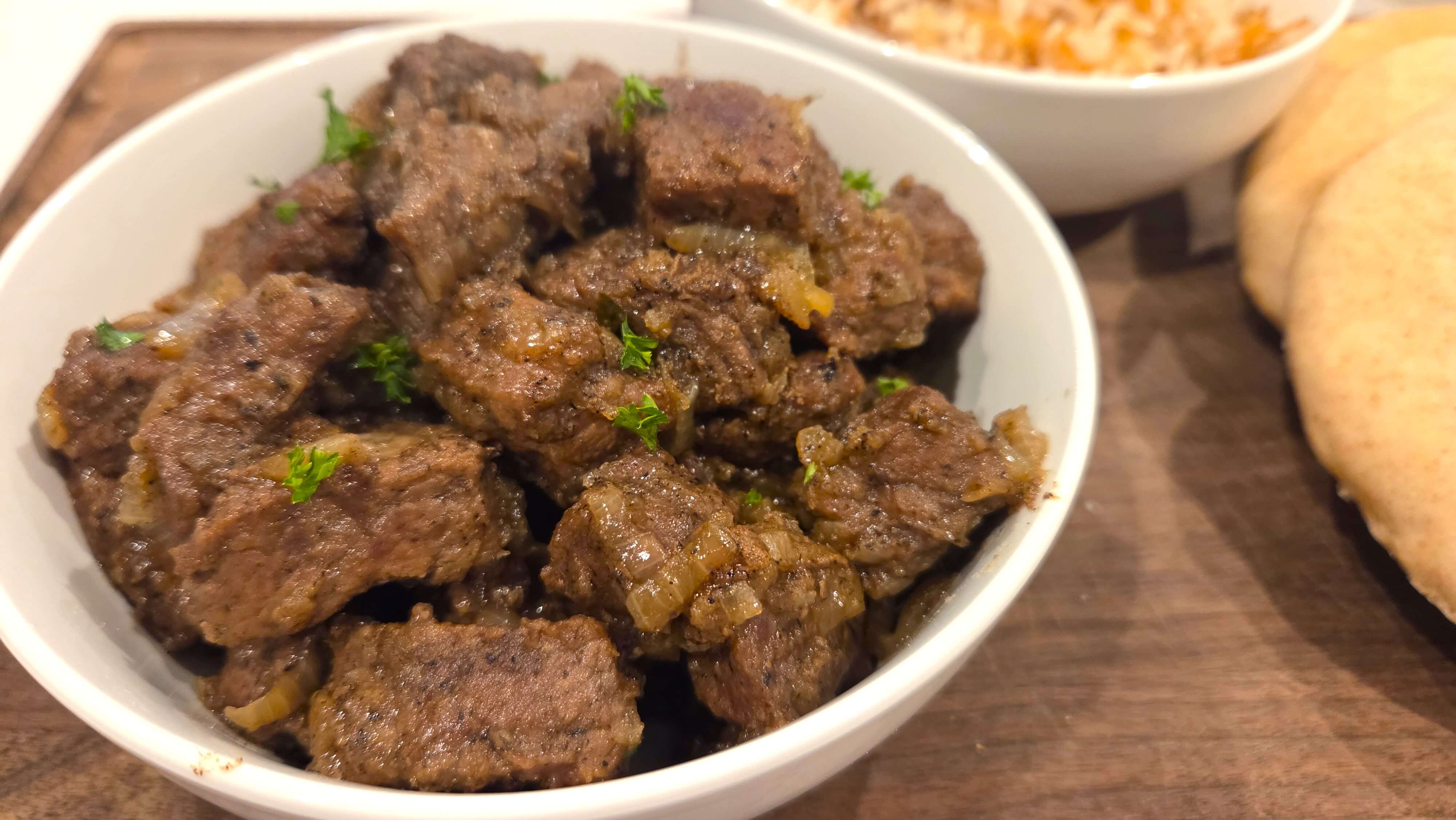 A premium close-up shot of a perfectly tender, juicy cubes of beef chuck in a deep bowl of authentic Kabab Halla, showing the thick caramelized onion sauce.