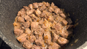 Cubed beef browning in a pot for Egyptian peas and carrots stew