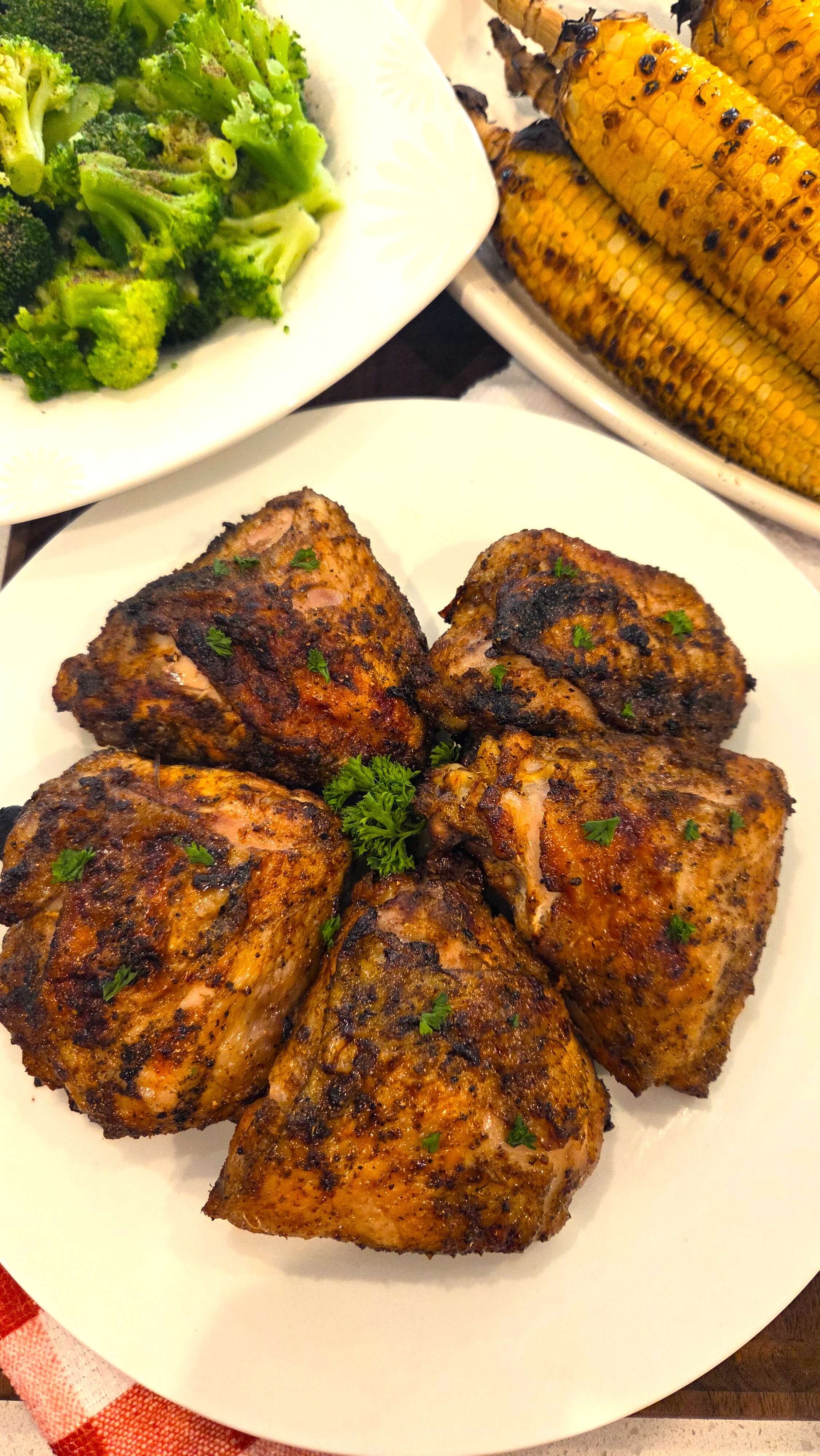 A premium close-up shot of grilled chicken thighs showing perfectly charred, crispy skins and a garnish of freshly chopped parsley.