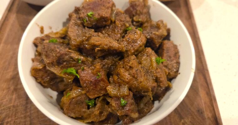 A wide overhead shot of a heavy ceramic bowl filled with hot Egyptian Kabab Halla braised beef and caramelized onion gravy on a rustic dining table.