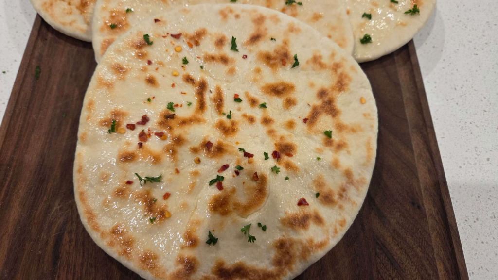 Homemade Turkish bazlama bread stacked on a cutting board with golden brown bubbles