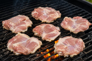 Raw chicken thighs skin-side down on a hot grill before cooking.