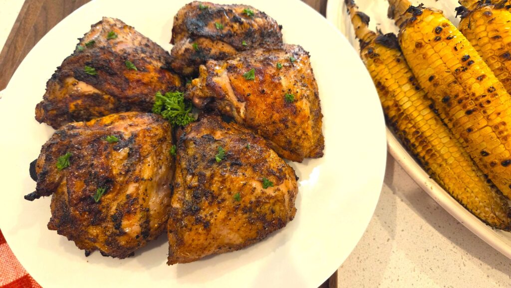 A beautiful platter of juicy, charred Middle Eastern grilled chicken thighs served hot alongside golden grilled corn on the cob.