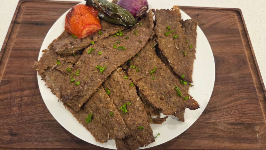 A beautiful top-down shot of paper-thin shavings of savory oven-baked Doner Kebab beef piled neatly on a clean white ceramic plate.