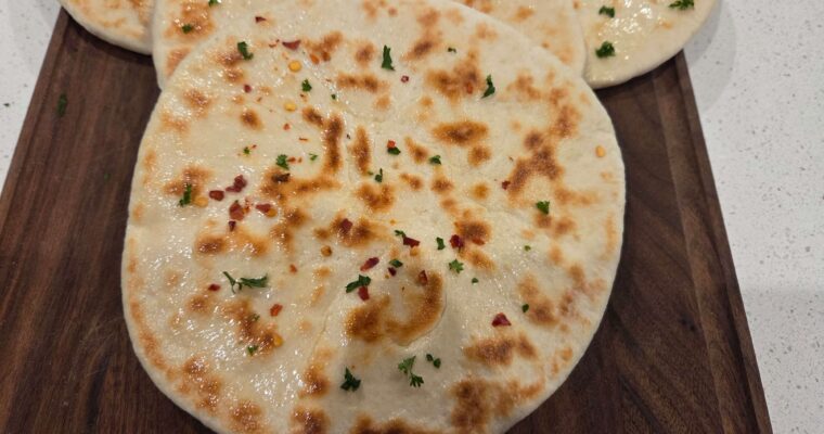A wide overhead shot of a stack of soft Turkish flatbreads with milk on a wooden cutting board.