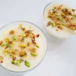 A wide overhead shot of traditional Egyptian mahalabia milk pudding cups chilled and garnished with chopped pistachios.