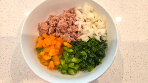 Chopped bell peppers, onion, and parsley added to a bowl of tuna for Mediterranean tuna salad.