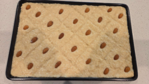 Vegan basbousa scored into squares and topped with almonds before baking.