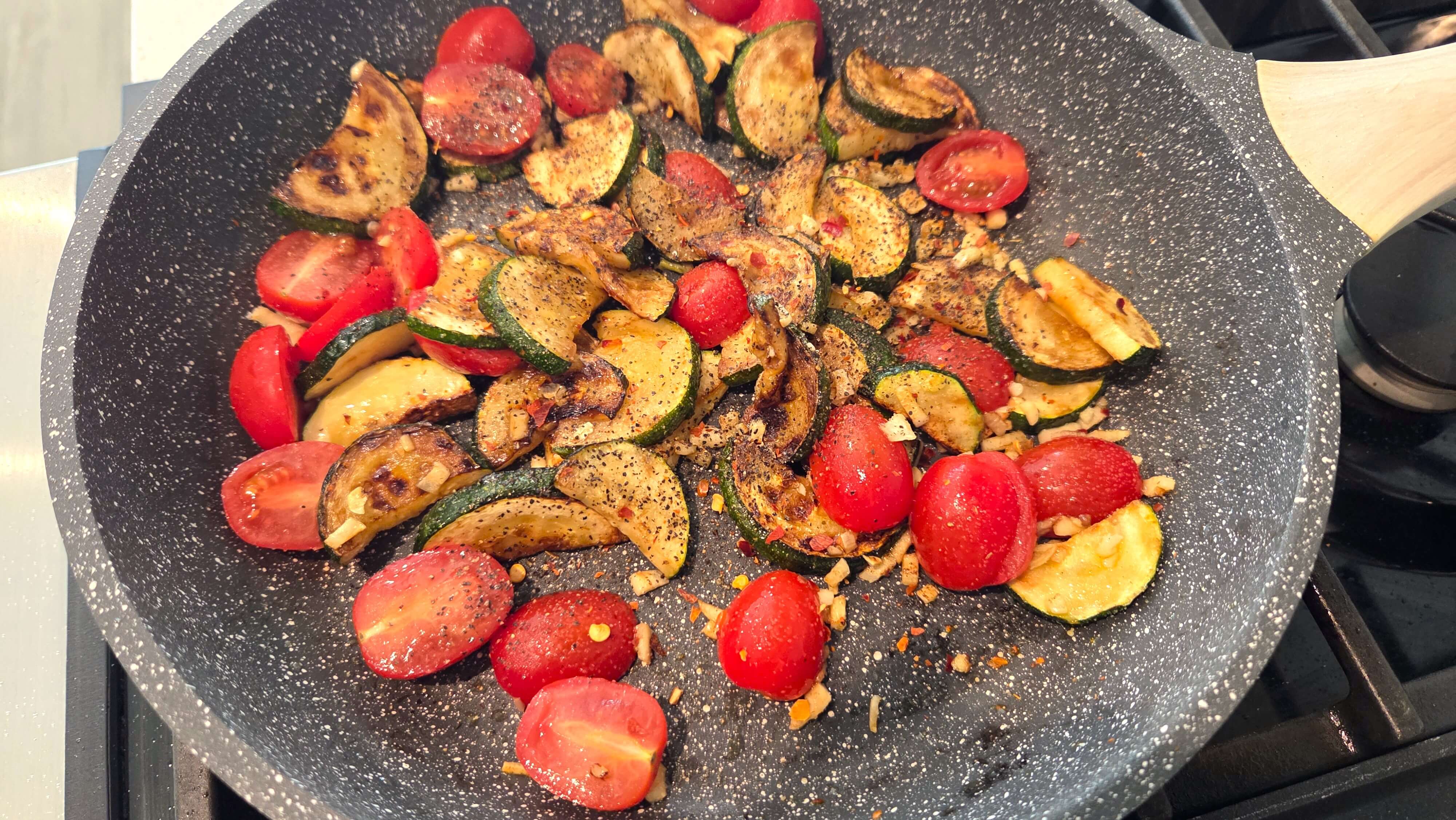 Cherry tomatoes cooking with zucchini, garlic, basil, and olive oil