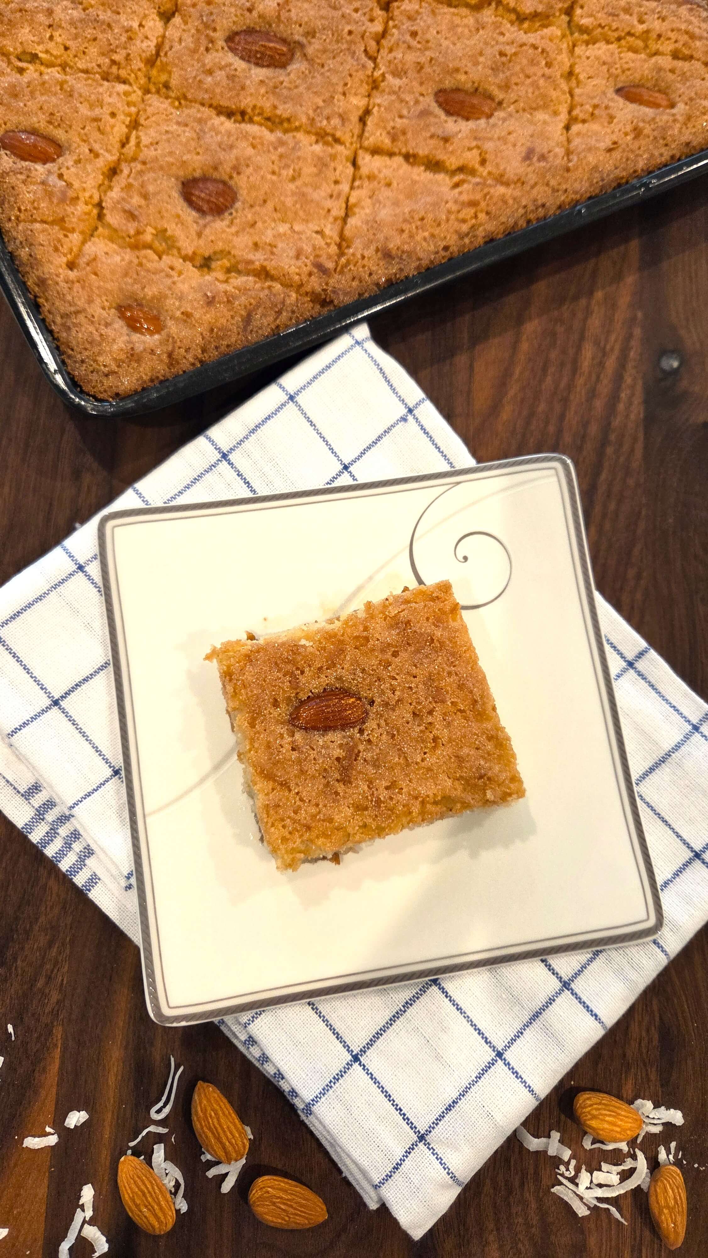 A premium close-up shot of a homemade vegan basbousa cake showing a moist semolina texture, crispy golden edges, and a whole blanched almond in the center.