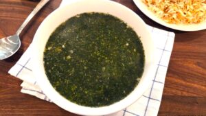 A wide overhead shot of a traditional bowl of velvety green Egyptian molokhia soup served hot.