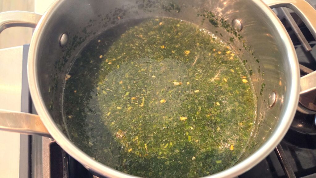 A close-up shot of a hot pot of Egyptian molokhia soup highlighting the sizzling garlic and coriander tasha on the surface.