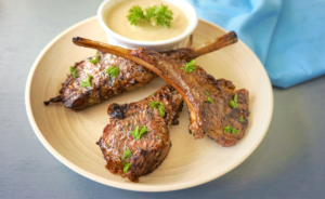 Mediterranean grilled lamb chops served on a platter with parsley and tahini sauce.