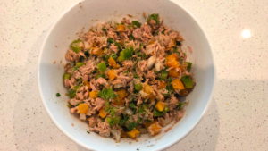 Mediterranean tuna salad being tossed together with olive oil dressing, vegetables, and herbs.