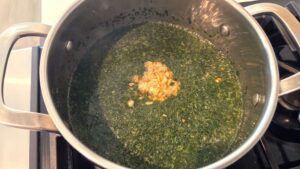 Garlic and coriander tasha being added to cooked molokhia