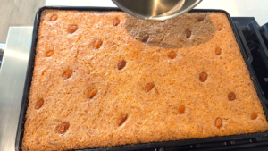 Pouring lemon syrup over hot vegan basbousa after baking.
