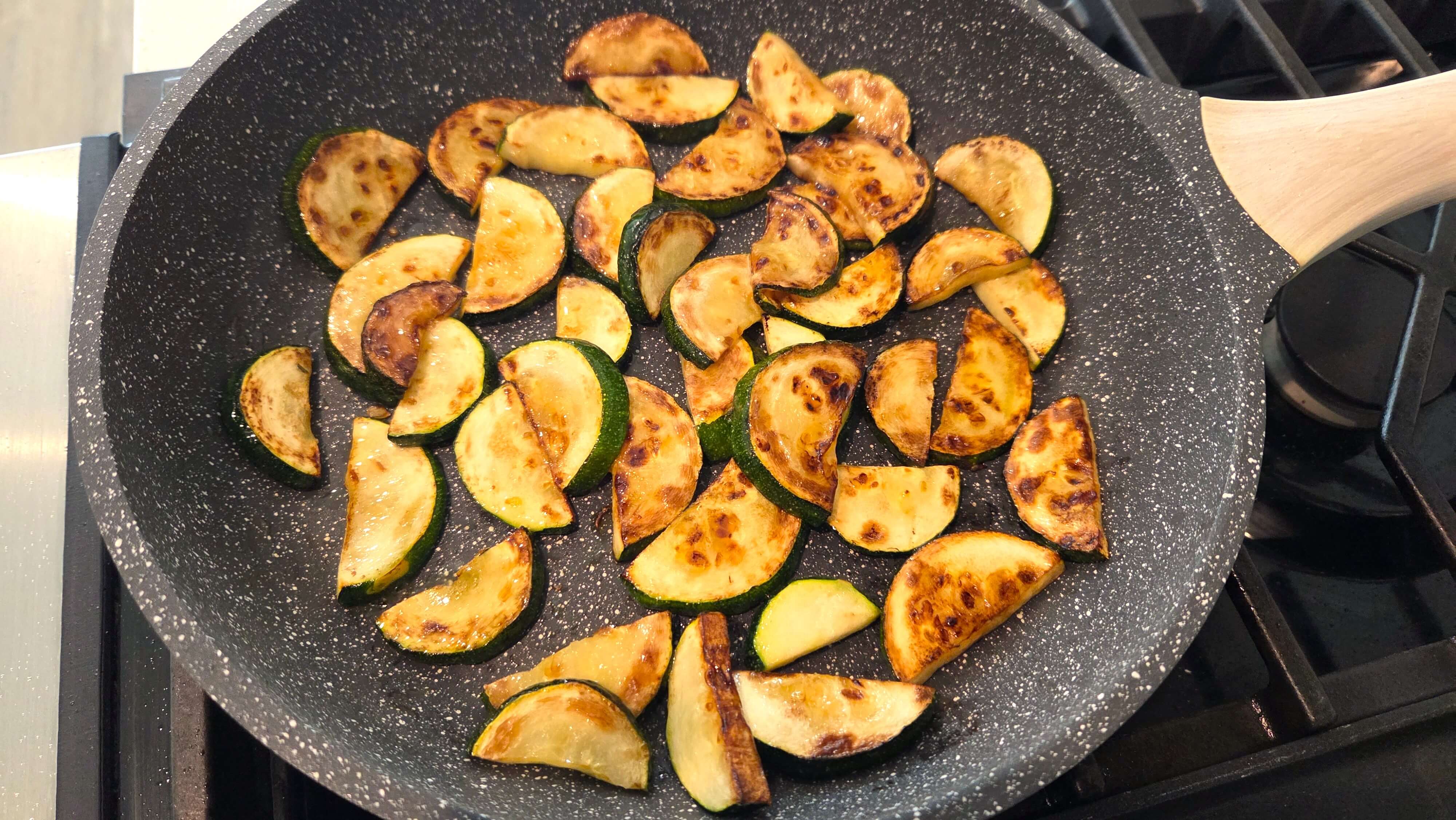 Sliced zucchini sautéing in olive oil until lightly golden.