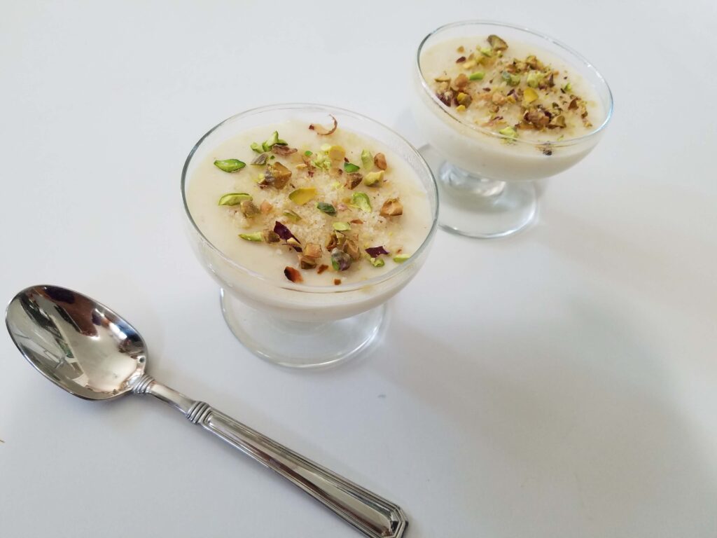 A top-down shot of a velvety bowl of Egyptian mahalabia milk pudding served cold and garnished with crunchy chopped pistachios.