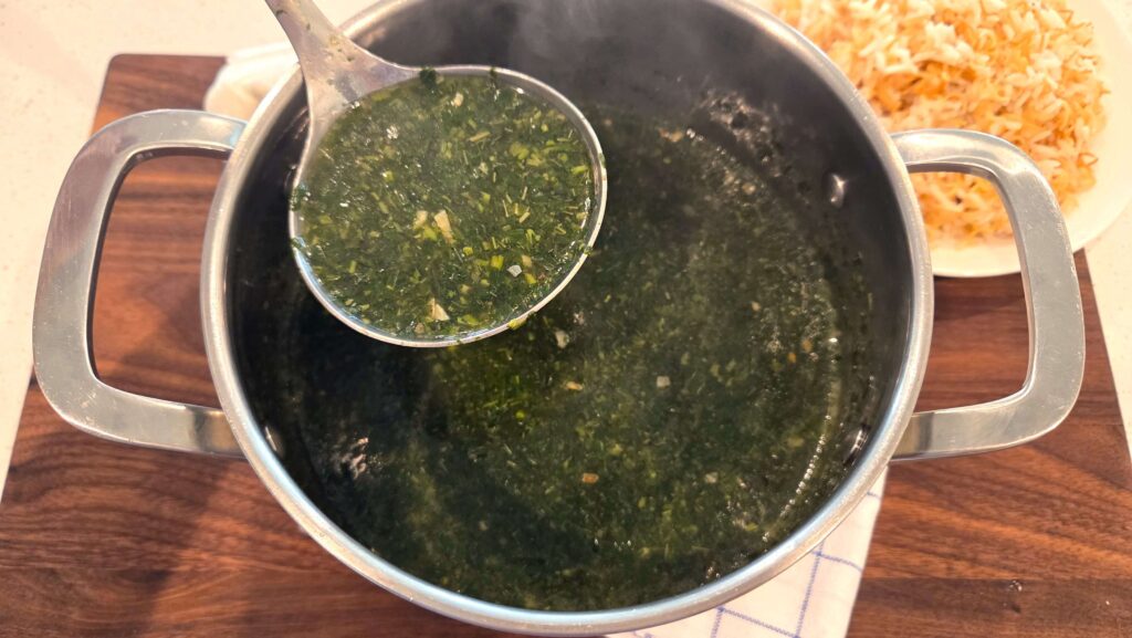 A top-down shot of a traditional pot of green molokhia soup served alongside a platter of golden vermicelli rice.