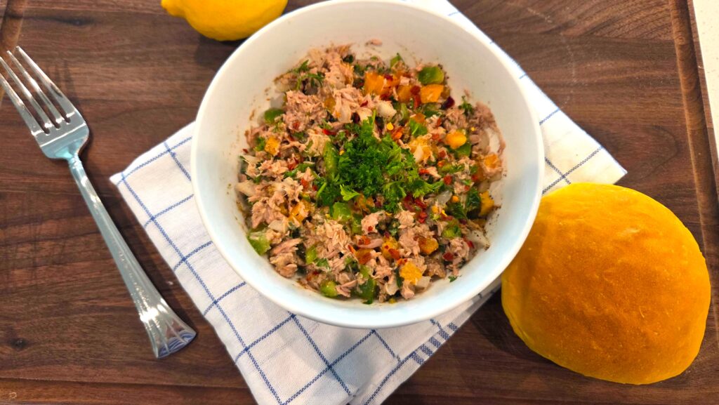 A beautiful top-down shot of crisp no mayo Mediterranean tuna salad served next to a warm bun on a clean plate.