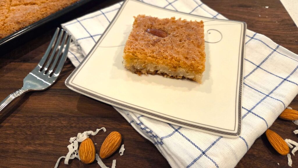 A beautiful top-down shot of a sliced diamond piece of vegan basbousa semolina cake served on a white ceramic plate.