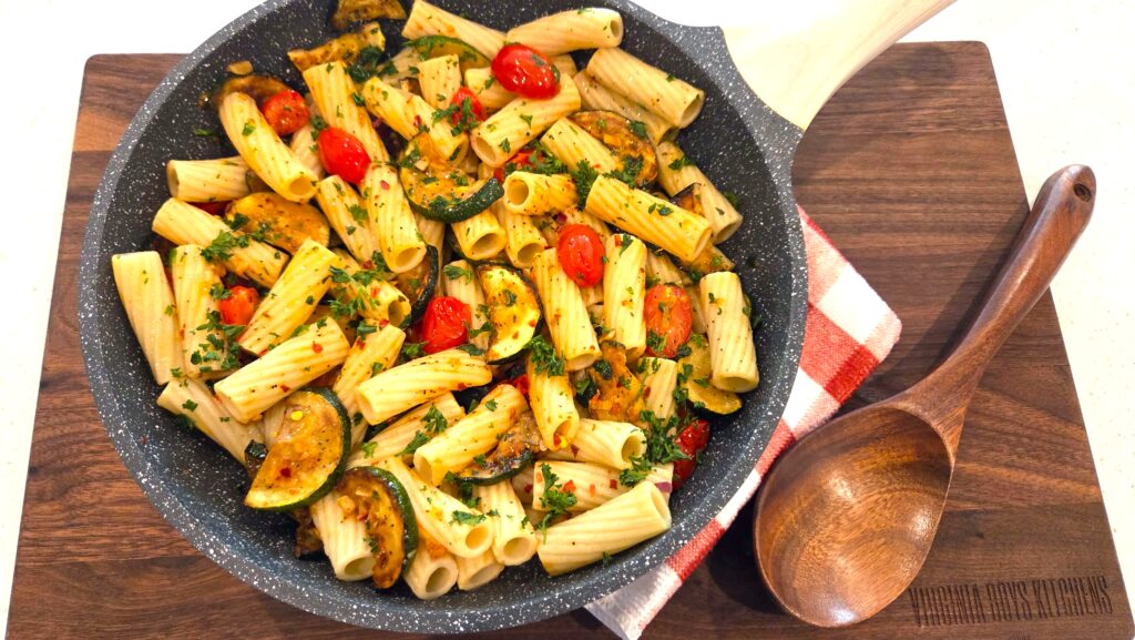 A top-down shot of a skillet of zucchini and cherry tomato pasta served hot.