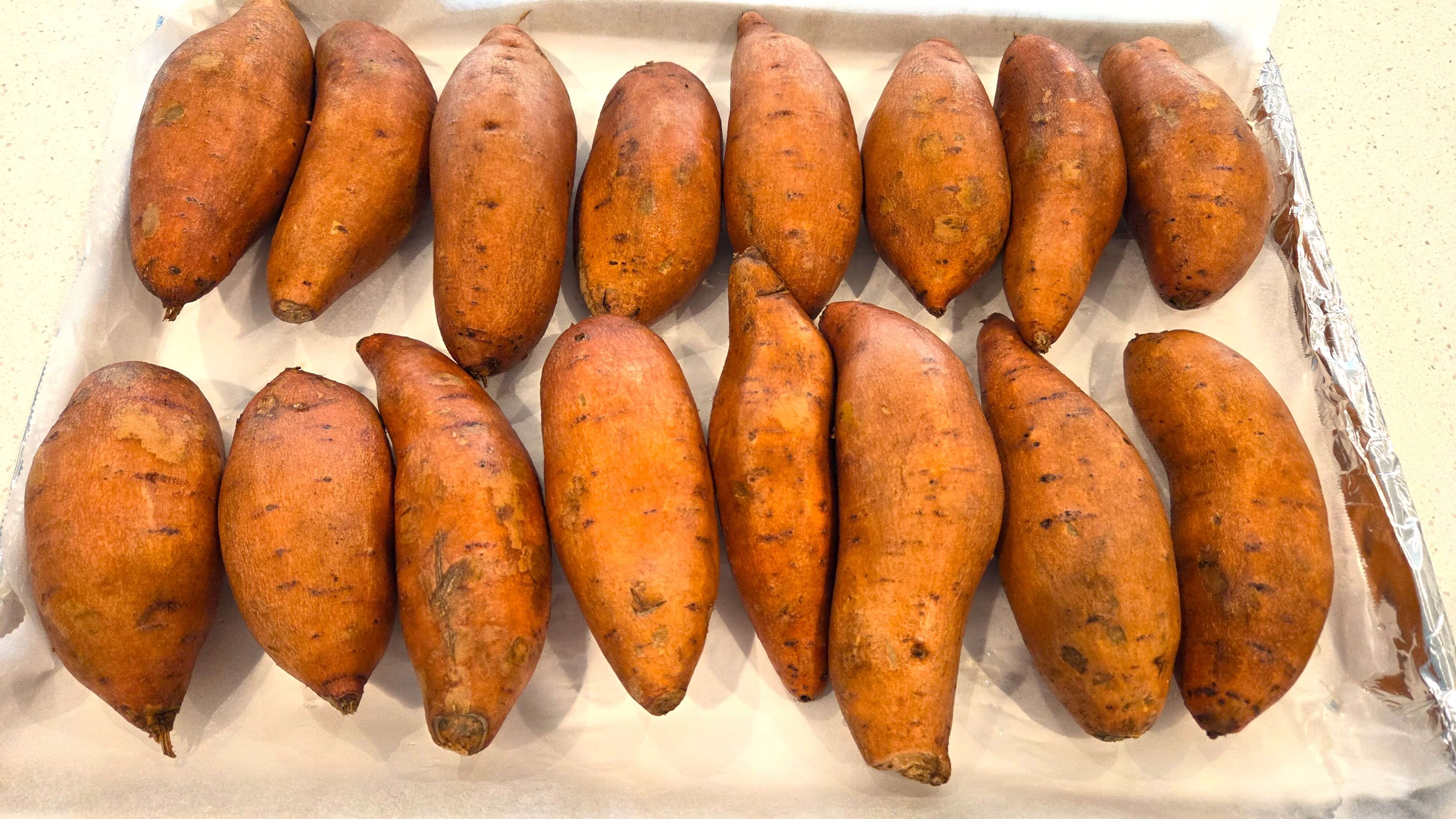 Whole sweet potatoes arranged on a baking sheet before baking
