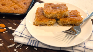 Slice of vegan Egyptian basbousa served on a plate with sweet lemon syrup and almonds.